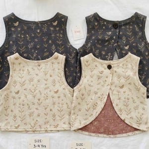 May include: Four children's vests with floral and bird patterns. Two vests are dark gray with a brown floral design, and two are beige with a brown floral design. The vests have a button closure in the back and are labeled with size ranges.