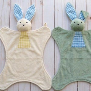 May include: Two baby security blankets, each featuring a plush bunny head and ears with a gingham pattern. One blanket is cream-colored with yellow gingham, the other is sage green with blue gingham. The blankets have a unique shape.