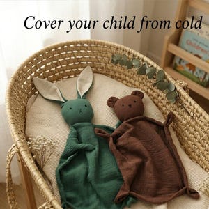 May include: A green bunny and brown bear security blanket set inside a woven basket. The bunny has long ears and the bear has small ears. The text "Cover your child from cold" is at the top of the image.