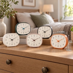 May include: Five oval-shaped analog alarm clocks in white, dark green, black, light pink, and orange. Each clock features a white face with black Arabic numerals, black hands, and a 14 cm width, 12 cm height, and 4.5 cm thickness measurement.
