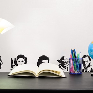 May include: A desk setup featuring a white desk lamp, an open book, a globe, and a pencil holder. Black and white character silhouettes are on the wall. The globe is blue and has a black stand.