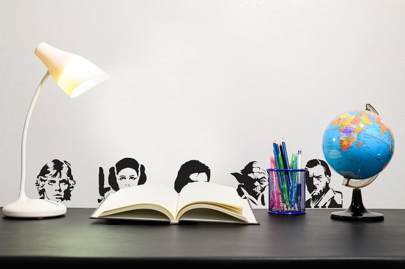 May include: A desk setup featuring a white desk lamp, an open book, a globe, and a pencil holder. Black and white character silhouettes are on the wall. The globe is blue and has a black stand.