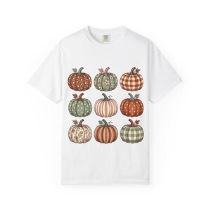 Peut inclure: Un t-shirt blanc à manches courtes avec une impression graphique de neuf citrouilles disposées en grille de trois par trois. Chaque citrouille présente un motif unique, incluant des pois, des rayures, des fleurs, des cœurs et des carreaux.