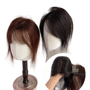 May include: Two hair toppers displayed on mannequin heads, one in a medium brown shade and one in black, both featuring wispy bangs. A circular inset shows the underside of a black hair topper with a small clip attached to the base mesh fabric.