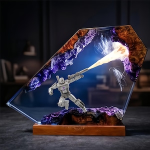 May include: A gray action figure of a robot firing a weapon, encased in a clear resin block. The resin features brown, purple, and blue accents, with a wooden base. The weapon emits a yellow beam.