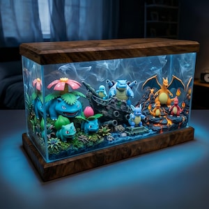 Puede incluir: Un terrario decorativo con marco de madera y una carcasa de vidrio transparente. En el interior, varias figuras de Pokémon están dispuestas en medio de un paisaje en miniatura con plantas, agua y roca volcánica. La escena está iluminada con luz azul.