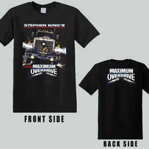 May include: A black short-sleeve t-shirt featuring a graphic print of a semi-truck with the text Stephen King's Maximum Overdrive on the front. The back of the shirt displays the Maximum Overdrive logo in white and blue lettering on a black background.
