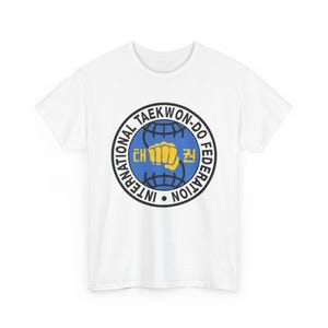 Puede incluir: Camiseta blanca con un emblema circular con el texto "INTERNATIONAL TAEKWON-DO FEDERATION". El emblema incluye un globo azul, un puño amarillo y caracteres coreanos. La camiseta está hecha de un material suave y ligero.