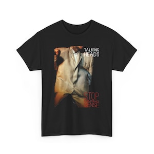 May include: A black short-sleeve t-shirt featuring a graphic print of a person wearing an oversized light-colored suit. The text TALKING HEADS appears in white at the top right, and the text STOP MAKING SENSE appears in red at the bottom right.