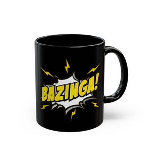 Op de afbeelding: Een zwarte keramische mok met een grafische afbeelding in stripstijl met het woord BAZINGA! in gele letters. De tekst is geplaatst tegen een witte en zwarte explosievorm met gele bliksemschichten die vanuit het midden van het ontwerp stralen.