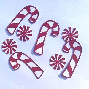 May include: A collection of red and white candy canes and peppermint candies. The candy canes are curved with red and white stripes. The peppermint candies are round with red and white stripes radiating from the center. The items are arranged on a white background.