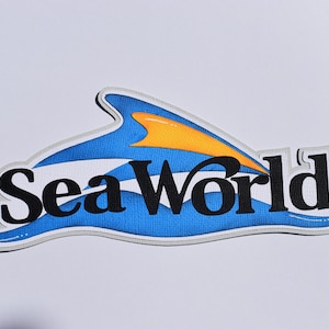 May include: SeaWorld logo featuring a blue and orange dolphin fin with the text "SeaWorld" in black.