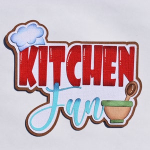May include: A brown and white sign with the text "Kitchen Fun" in red and blue lettering. A chef's hat is in the upper left corner of the sign. A brown bowl with a wooden spoon is in the lower right corner of the sign.