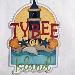 May include: A layered paper craft featuring a lighthouse, the text "TYBEE Island", seashells, starfish, and a dolphin. The lighthouse is blue and tan, set against a yellow sun. The text is red and green, with a blue and tan ocean scene.