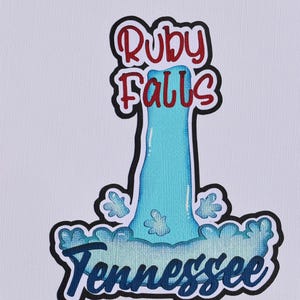 May include: A colorful illustration of Ruby Falls in Tennessee. The image features the text "Ruby Falls" in red and "Tennessee" in blue, with a waterfall design in shades of blue and white. The artwork is outlined in black.