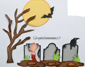 Może przedstawiać: Halloweenowy projekt rękodzieła z żółtym księżycem w pełni, czarnym nietoperzem i nagim drzewem. Scena zawiera szare nagrobki, rękę zombie i czarnego kruka. Obecny jest również tekst "Scrapbookinmomma13".