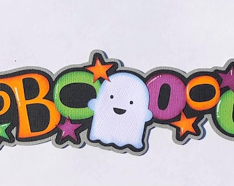 Puede incluir: Un cartel de "BOO" colorido con un fantasma y estrellas. Las letras son naranja, verde y morado con contornos negros. El fantasma es blanco con una sonrisa negra.