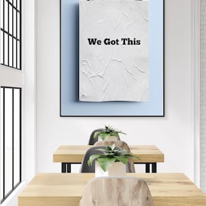 Può includere: Un poster incorniciato con la scritta "We Got This" è appeso a una parete azzurra. Sotto, sono disposti tre tavoli in legno con gambe in metallo nero e sedie in legno. Ogni tavolo ha una pianta in vaso.
