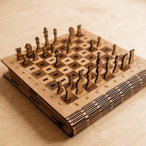 May include: A wooden chess set with laser-cut pieces and a board. The chess pieces are in a natural wood color, and the board has a grid pattern. The set is on a light-colored wooden surface.
