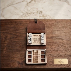 May include: A wooden Farkle dice game set with a leather case, dice, and a scoring chart. The set includes six white dice with black dots, a brown leather case, and a wooden scoring board. The game is displayed on a dark wooden surface.