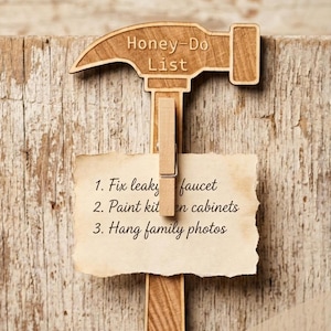 May include: A light brown wooden hammer-shaped wall mount featuring the text Honey-Do List. A wooden clothespin is attached to the center, holding a piece of aged paper with the text: 1. Fix leaky faucet, 2. Paint kitchen cabinets, 3. Hang family photos.