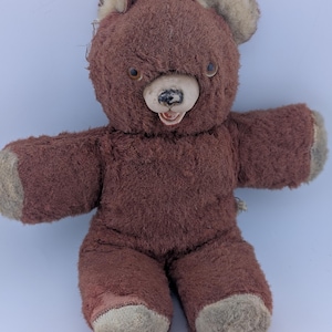 Può includere: Un orsacchiotto vintage con pelliccia testurizzata marrone scuro e accenti beige più chiari su orecchie, zampe e piedi. L'orso presenta un viso modellato di colore chiaro con un naso dipinto di nero, una piccola bocca aperta e occhi scuri.