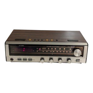 Puede incluir: Un radio reloj electrónico Sears FM estéreo AM con una parte superior de grano de madera y un panel frontal plateado. El dispositivo cuenta con una pantalla digital, un dial de sintonización analógico horizontal, botones y cuatro perillas de control.