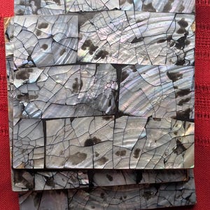 May include: A stack of square coasters featuring a mosaic inlay of iridescent gray and silver mother-of-pearl shell fragments. Each piece displays a cracked, web-like pattern with dark gray inclusions and a shimmering, reflective surface finish.