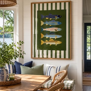 May include: A rectangular framed wall art piece featuring a vertical stack of five stylized fish illustrations in blue, yellow, and orange tones, set against a dark green background with a white and dark green vertical striped border.