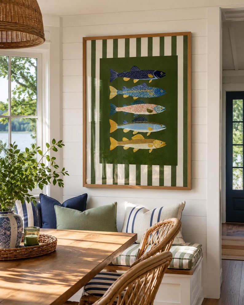 May include: A rectangular framed wall art piece featuring a vertical stack of five stylized fish illustrations in blue, yellow, and orange tones, set against a dark green background with a white and dark green vertical striped border.