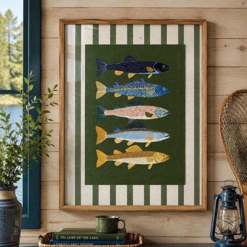 May include: A framed wall art piece featuring five stylized fish illustrations stacked vertically on a dark green background. The artwork is set against a cream and dark green striped matting within a light wood frame, showcasing fish in shades of dark blue, light blue, orange, and yellow.
