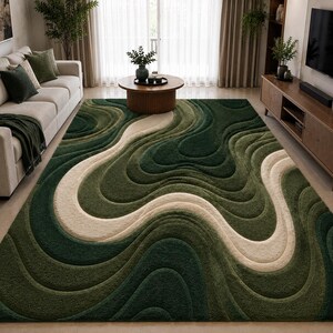 May include: A large, green area rug with a flowing, layered design. The rug features shades of green and a cream-coloured, wave-like pattern. The rug is placed in a living room setting with a sofa, coffee table, and entertainment unit.