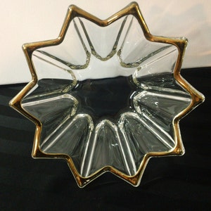 Puede incluir: Un cuenco de vidrio transparente en forma de estrella con un borde dorado. El cuenco es perfecto para servir aperitivos o para guardar objetos pequeños.