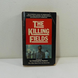 Puede incluir: Una portada de libro de bolsillo con fondo rojo y el título "The Killing Fields" en texto blanco. El libro es una novela de Christopher Hudson y está basado en la película del mismo nombre.