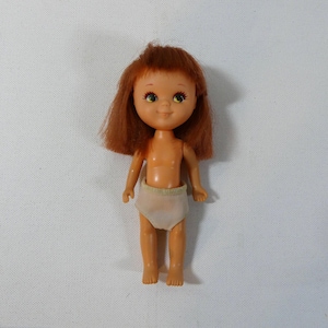 May include: A small plastic doll with brown hair, wearing a white diaper. The doll has painted on eyes and a smile.