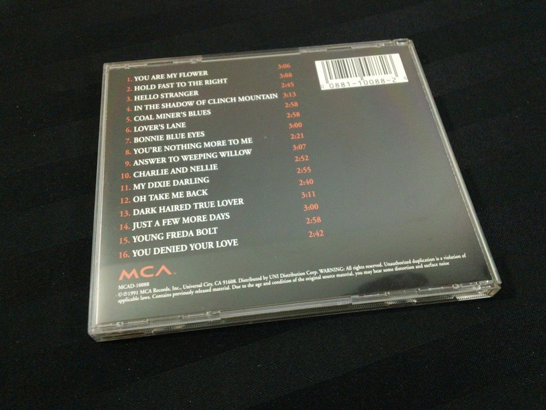 May include: A compact disc case with a black background and a list of song titles. The titles include "You Are My Flower" and "Bonnie Blue Eyes." The case has a clear plastic cover.