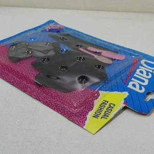 May include: A plastic package with a pink and blue background. The package contains a black and gray outfit for a doll. The package also includes a pink and white comb and a white and pink hairbrush. The package says "Diana Casual Fashion" on the front.