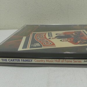 May include: A CD case featuring "The Carter Family" album cover. The cover art displays a vintage design with the band's name and images of the musicians. The case is clear with a black base and includes the text "Country Music Hall of Fame Series".