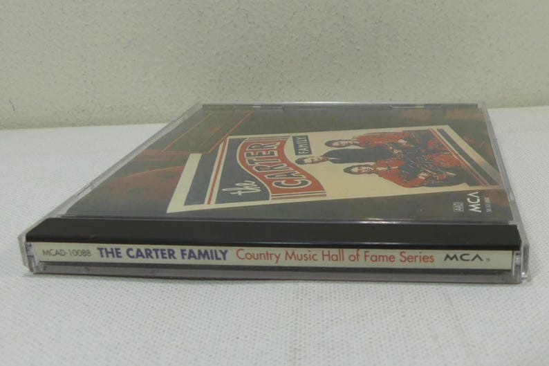 May include: A CD case featuring "The Carter Family" album cover. The cover art displays a vintage design with the band's name and images of the musicians. The case is clear with a black base and includes the text "Country Music Hall of Fame Series".
