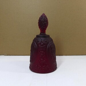 May include: A deep red glass bell with a textured surface and a decorative top. The bell has a vintage look and is made of glass.
