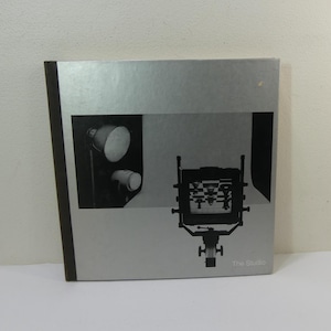 May include: A black and white photograph of a camera and lighting equipment. The image is from a book titled "The Studio".