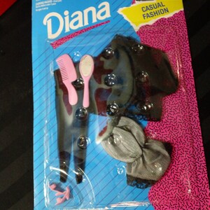 May include: A plastic package containing a doll outfit with a black and white top, a gray skirt, a pink comb, a pink hairbrush, and a pair of pink shoes. The package is labeled "Diana Casual Fashion".