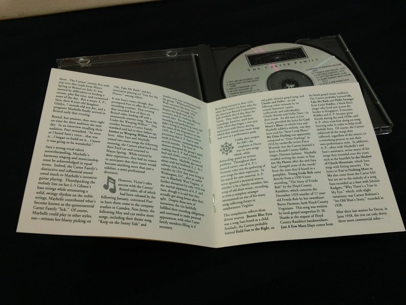 May include: A CD case with a compact disc inside and an open booklet. The disc has text that reads "The Carter Family". The booklet has text and a musical note graphic. The case is on a dark surface.