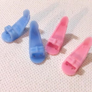 以下が含まれることがあります： プラスチック製のドールシューズが4足。2足はピンク、2足は薄いブルー。シューズはすべて同じスタイルで、トップにストラップがあり、小さなヒールがあります。