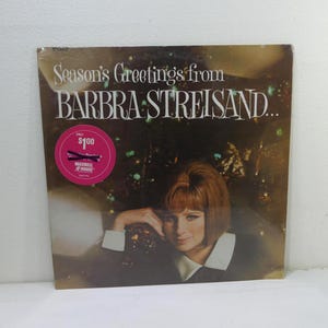 Op de afbeelding: Vintage vinyl albumhoes voor "Season's Greetings from Barbra Streisand". De hoes toont een portret van Barbra Streisand met witte tekst. Aan de linkerkant zit een roze sticker met tekst.
