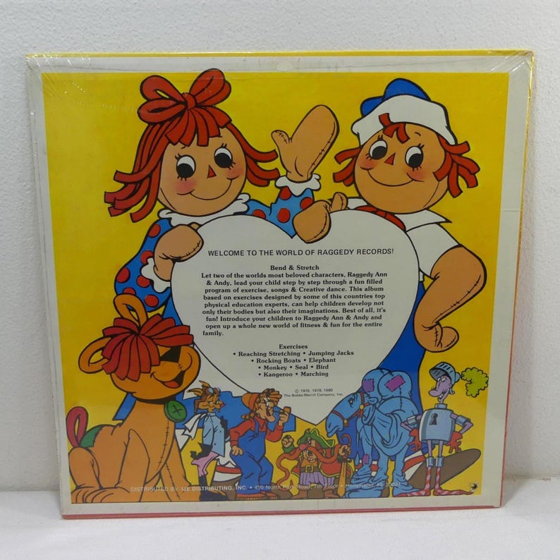 May include: A vintage record album cover featuring Raggedy Ann and Andy, two iconic rag dolls. The cover is red, white, and blue with a heart-shaped design. The text on the cover reads "Welcome to the World of Raggedy Records!" and "Bend & Stretch". The album features a program of exercise, songs, and creative dance for children.