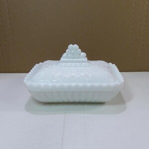 Puede incluir: Un plato blanco rectangular con tapa y un patrón floral texturizado. La tapa presenta un grupo de pequeños acentos redondos. El plato tiene un borde festoneado y una base acanalada. Una pieza decorativa para el hogar.