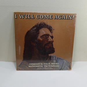 Puede incluir: Una portada de álbum de vinilo vintage con una pintura de un hombre con barba sobre un fondo marrón. El título del álbum es "I Will Come Again!" y el texto debajo dice "composed by Guy E. Shirley performed by The Trinteens".