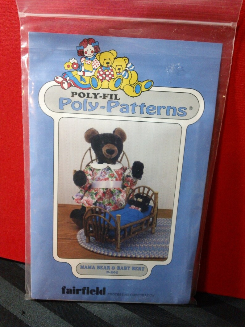 May include: A blue package featuring a bear pattern. The package has the text "POLY-FIL Poly-Patterns" and "MAMA BEAR & BABY BERT". The image shows a black bear wearing a floral dress and a baby bear in a wooden bed. The package is in a clear plastic bag.