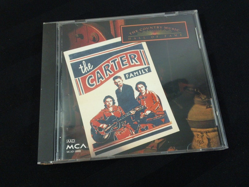 May include: A CD case featuring "The Carter Family" album cover. The cover art includes a vintage photograph of the musical group with the text "The Country Music Hall of Fame". The CD case is clear plastic.